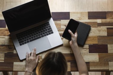 Kadın eli bilgisayarlı akıllı telefon kullanır. İnternette çalış ve çalış, serbest çalış. Serbest çalışan ya da serbest çalışan bir kadın, dizüstü bilgisayarıyla çalışan bir kız ahşap masada oturan bir telefon ve okuyucu..