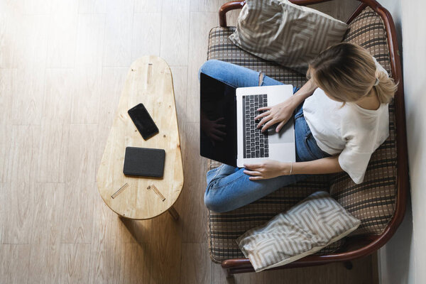 Woman with a laptop sitting on a sofa. Study and work online, freelance. Self employed woman, girl working with her notebook sitting on a couch with a phone, smartphone and ereader on table.