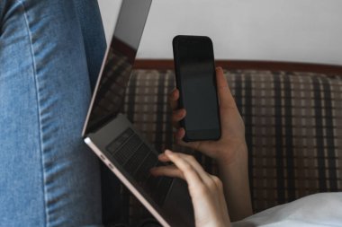 Dizüstü bilgisayarı olan bir kadın kanepede uzanıyor ve akıllı telefon kullanıyor. İnternette çalış ve çalış, serbest çalış. Defteriyle çalışan serbest çalışan bir kız elinde telefonuyla kanepede yatıyor..