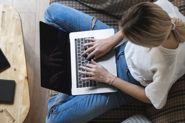 Woman with a laptop sitting on a sofa. Study and work online, freelance. Self employed woman, girl working with her notebook sitting on a couch with a phone, smartphone and ereader on table.