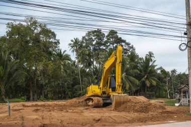 Mavi gökyüzüne karşı bir inşaat alanında sarı kazıcı. Ağır endüstri. Endüstriyel kazıcının detaylarını kapat. Arka planda avuç içleri olan turuncu bir zeminde duran büyük bir iz kazıcı..