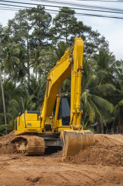 Mavi gökyüzüne karşı bir inşaat alanında sarı kazıcı. Ağır endüstri. Endüstriyel kazıcının detaylarını kapat. Arka planda avuç içleri olan turuncu bir zeminde duran büyük bir iz kazıcı..