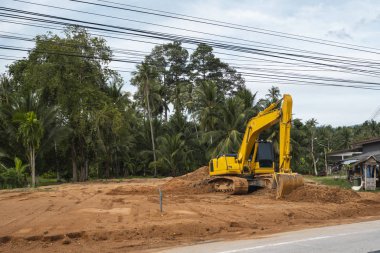 Mavi gökyüzüne karşı bir inşaat alanında sarı kazıcı. Ağır endüstri. Endüstriyel kazıcının detaylarını kapat. Arka planda avuç içleri olan turuncu bir zeminde duran büyük bir iz kazıcı..