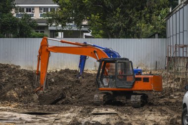 İnşaat alanında çalışmak için mavi gökyüzü ve denize karşı bir zeminde turuncu kazıcı. Arka planda mavi bir deniz bulunan küçük bir kazıcı. Ağır sanayi.