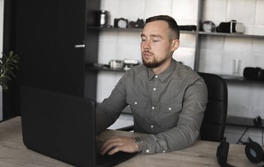 Genç işadamı ya da öğrenci bilgisayar monitörü karşı oturan bir gömlek. Düşünceli bir ifade ile ofiste bir masada bir pc üzerinde çalışıyor. Ofiste dizüstü bilgisayar üzerinde çalışan genç işadamı.