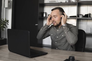 Genç işadamı ya da bir gömlek öğrenci kulaklık bilgisayar monitörü karşı oturan. Düşünceli bir ifade ile ofiste bir masada bir pc üzerinde çalışma.