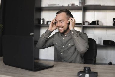 Mutlu gülümseyen Genç işadamı ya da öğrenci bir gömlek kulaklık bilgisayar monitörü karşı oturan ve internet üzerinden biriyle konuşan. Ofisteki bir masada bir bilgisayar üzerinde çalışmak.