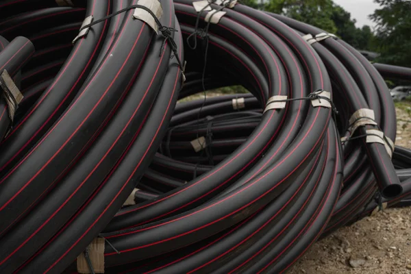 Rury z czarnej gumy lub tworzywa sztucznego z czerwonymi liniami jako materiałem budowlanym i wyposażeniem na placu budowy. Użycie jako rury wodnej. — Zdjęcie stockowe