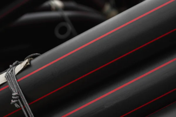 Schwarze Gummi- oder Kunststoffrohre mit roten Linien als Baumaterial und Ausrüstung auf der Baustelle. Verwendung als Wasserleitung. — Stockfoto