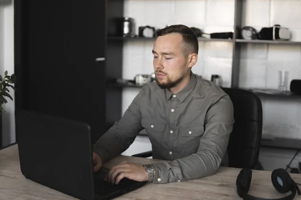 年轻的商人或学生穿着衬衫坐在电脑显示器上。在办公室的桌子上用一张电脑，用深思熟虑的表情。年轻的商人在办公室工作，他的笔记本电脑. — 图库照片
