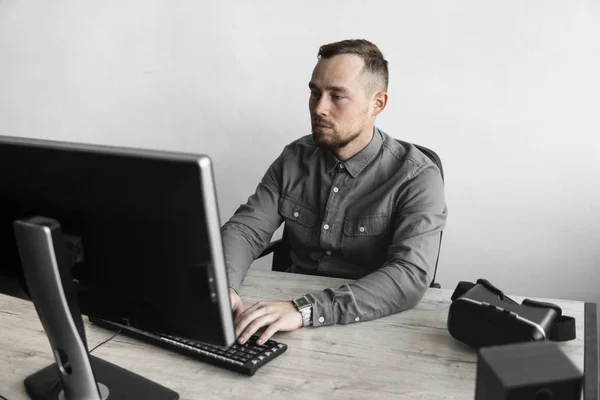 Νέος επιχειρηματίας ή μαθητής σε ένα πουκάμισο που κάθεται ενάντια στην οθόνη του υπολογιστή. Δουλεύοντας σε έναν υπολογιστή σε ένα τραπέζι στο γραφείο με μια προσεκτική έκφραση. Νέος επιχειρηματίας που εργάζεται για το laptop του στο γραφείο. — Φωτογραφία Αρχείου