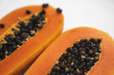 Beyaz bir tabakta tohum ile yarısı kesilmiş papaya. Beyaz arkaplanı olan tatlı papaya dilimleri. Yarım papayalar. Sağlıklı egzotik meyveler. Vejetaryen yemeği..