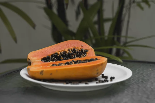 De helft van de rijpe papaya met zaad op een wit bord en met een groene plant op de achtergrond. Snijdt zoete papaja. Halve papaja 's. Gezonde exotische vruchten. Vegetarisch voedsel. — Stockfoto