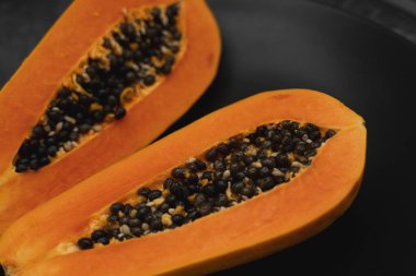 Olgun papayanın yarısı siyah tabakta tohum ve arka planda yeşil bitkiler. Tatlı papaya dilimleri. Yarım papayalar. Sağlıklı egzotik meyveler. Vejetaryen yemeği..