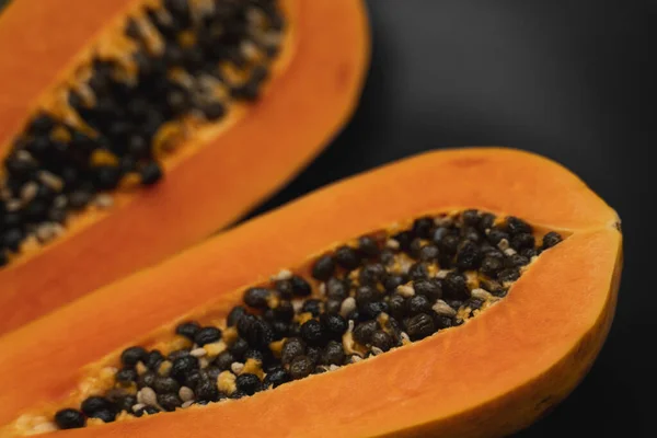 Half of ripe papaya with seed on a black plates and with a green plants on background. Slices of sweet papaya. Halved papayas. Healthy exotic fruits. Vegetarian food.