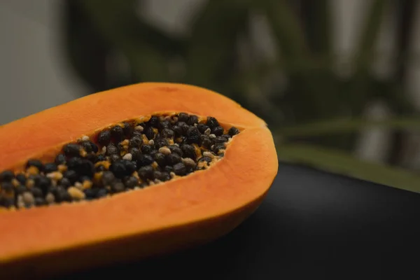 De helft van de rijpe papaya met zaad op een zwarte plaat en met een groene plant op de achtergrond. Snijdt zoete papaja. Halve papaja 's. Gezonde exotische vruchten. Vegetarisch voedsel. — Stockfoto