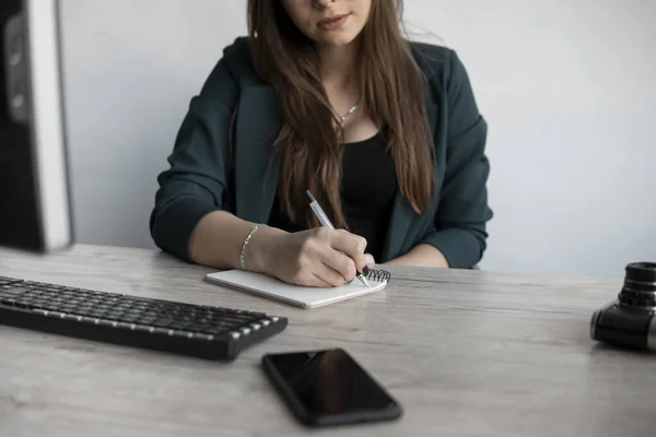 Biznesmenka pisze coś w notatniku. Rozpoczęcie kobieta przedsiębiorca student studiuje pisanie notatek w miejscu pracy w pobliżu komputera. Kobieca ręka zapisująca na białym pustym notesie na stole. — Zdjęcie stockowe