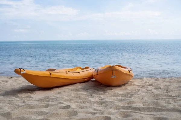 Two colorful orange kayaks on a sandy beach ready for paddlers in sunny day. Several orange recreational boats on the sand. Active tourism and water recreation.