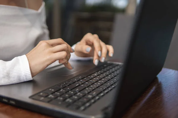 Hermosa mujer joven en camiseta blanca está trabajando en el ordenador portátil y sonriendo mientras se sienta al aire libre en la cafetería. Mujer joven usando el portátil para el trabajo. Freelancer femenina trabajando en un portátil en una cafetería al aire libre . — Foto de Stock