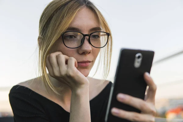 Young business woman uses phone. Good looking brunette female uses online banking on smart phone to transfer money from credit card. Girl using smart phone and chatting with business partners.