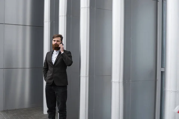 Businessman talking on the phone in financial district. Portrait of a Young urban professional man using smart phone over office building. Business man talking on his smartphone outdoors. Technology.