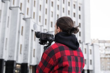 3 eksenli titreşimli dengeleyicide profesyonel kamera tutan genç profesyonel kameraman. Pro ekipmanlar titremeden yüksek kaliteli video çekmeye yardımcı olur. Kırmızı tişört giyen kameraman video çekiyor..