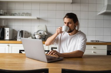 Evde çalışan ve dizüstü bilgisayar kullanan bir serbest çalışan. Yakışıklı, gülümseyen bir adam elinde kahve fincanıyla dizüstü bilgisayara bakıyor. Başarılı bir girişimci dizüstü bilgisayarla oturuyor ve kendi bilgisayarında çalışıyor.