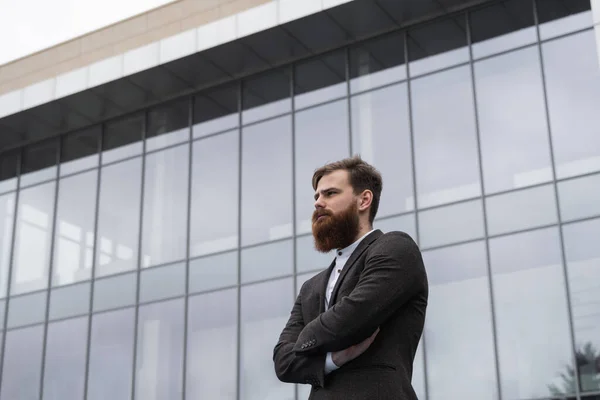 Portrait of an handsome businessman wearing jacket over office building in financial district outdoors. Young bearded Businessman outdoor. Successful entrepreneur dressed in formal wear.