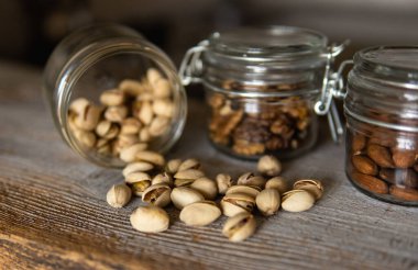 Fıstıklar bir kavanozdan beyaz şarap masasına saçılmış ve diğer fındıklar arka planda. Pistachio sağlıklı bir vejetaryen protein yiyeceğidir. Köhne odunlarda fıstıklar.