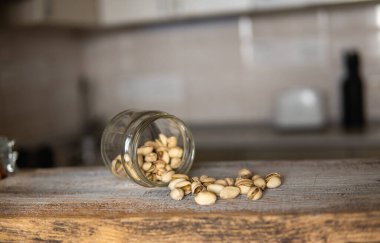 Fıstıklar bir kavanozun içindeki beyaz şarap masasına saçılmış. Pistachio sağlıklı bir vejetaryen protein yiyeceğidir. Köhne odunlarda fıstıklar.