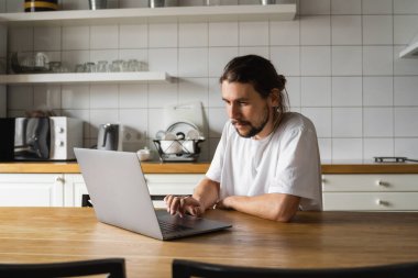 Evde çalışan ve dizüstü bilgisayar kullanan bir serbest çalışan. Laptopla çalışan ve iyi haberler okuyan sakallı bir adam. Yakışıklı başarılı girişimci modern evinde oturuyor ve çalışıyor..