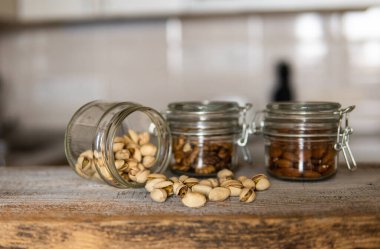 Fıstıklar bir kavanozdan beyaz şarap masasına saçılmış ve diğer fındıklar arka planda. Pistachio sağlıklı bir vejetaryen protein yiyeceğidir. Köhne odunlarda fıstıklar.