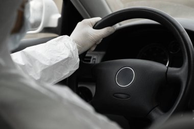 Koruyucu giysili, tıbbi maskeli ve plastik eldivenli bir adam bakteri ve virüsten korunmak için araba kullanıyor. Karantina sırasında koruyucu maske, dünya salgını, covid 19, koronavirüs, enfeksiyon.