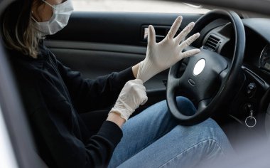 Koruyucu tıbbi maskeli kadın araba sürmeyi planlarken kendini bakteri virüsünden korumak için lastik eldiven takıyor. Karantina, salgın, covid 19, koronavirüs ve enfeksiyon sırasında koruyucu maske..
