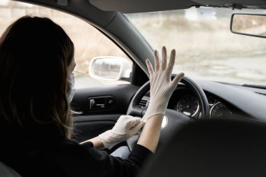 Koruyucu tıbbi maskeli kadın araba sürmeyi planlarken kendini bakteri virüsünden korumak için lastik eldiven takıyor. Karantina, salgın, covid 19, koronavirüs ve enfeksiyon sırasında koruyucu maske..