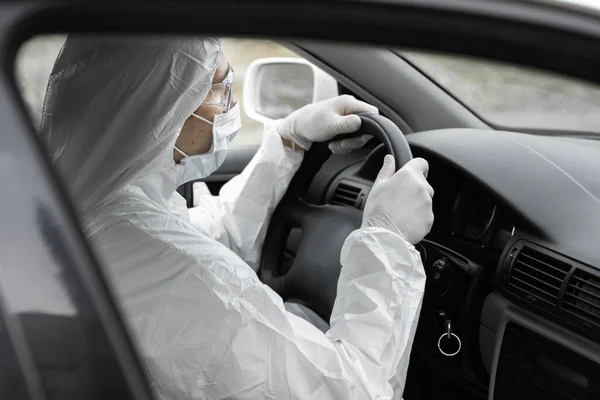 細菌やウイルスから保護するための保護スーツ、医療用マスクやゴム手袋の男は車を運転しています。隔離中の保護マスク世界的大流行covid 19コロナウイルス感染. — ストック写真
