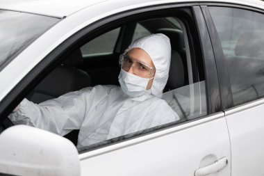 Koruyucu giysili, tıbbi maskeli ve plastik eldivenli bir adam bakteri ve virüsten korunmayı planlıyor. Karantina sırasında koruyucu maske, dünya salgını, covid 19, koronavirüs, enfeksiyon.