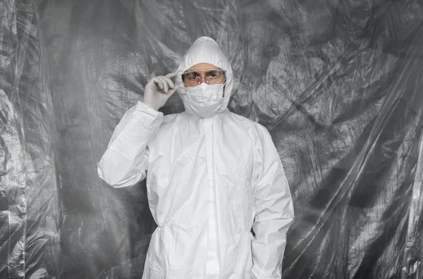 Arzt in weißem Schutzanzug, Maske, Brille und Gummihandschuhen steht bereit, um einem Volk zu helfen, während eine Coronavirus-Pandemie droht. Epidemie, Pandemie des Coronavirus covid 19. Arzt unter Atemschutz. — Stockfoto