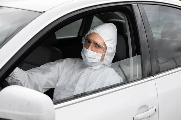 Человек в защитном костюме, медицинской маске и резиновых перчатках для защиты от бактерий и вирусов планирует водить машину. Защитная маска при карантине, мировая пандемия, ковид 19, коронавирус, инфекция . — стоковое фото
