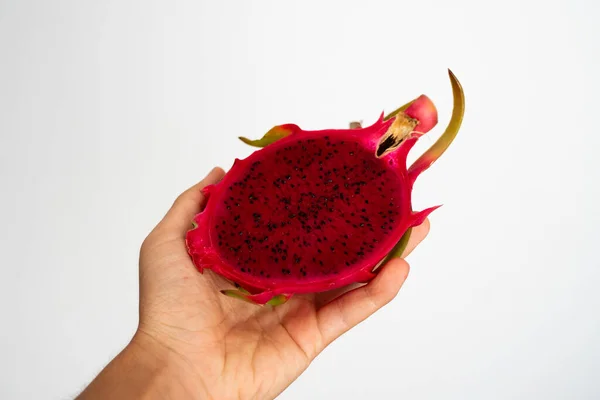 Manos femeninas sosteniendo la mitad de la fruta roja madura del dragón sobre fondo blanco . — Foto de Stock