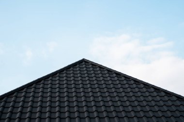 Siyah metal kiremit çatı. Çatı metal levhaları. Modern çatı malzemesi türleri. Evin çatısı, mavi gökyüzüne karşı metal çatı fayansı. İnşa ediliyor.