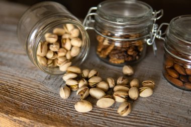 Fıstıklar bir kavanozdan beyaz şarap masasına saçılmış ve diğer fındıklar arka planda. Pistachio sağlıklı bir vejetaryen protein yiyeceğidir. Köhne odunlarda fıstıklar.