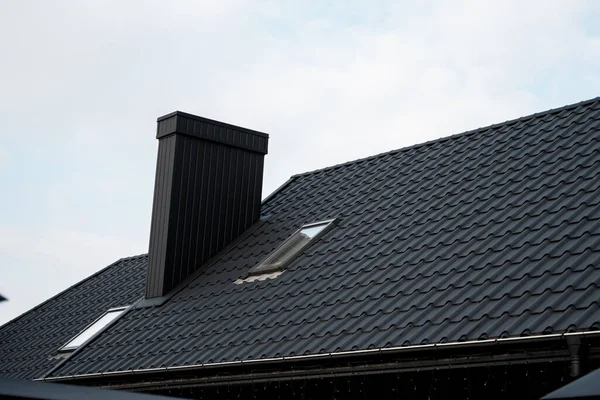 Schwarzes Ziegeldach. Dachbleche. Moderne Arten von Dachmaterialien. Dach des Hauses, Dachziegel aus Metall gegen den blauen Himmel. Bauen. — Stockfoto