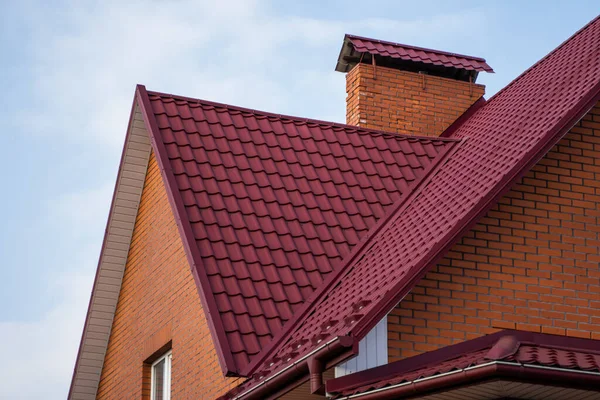 Červená kovová střecha. Střešní plechy. Moderní typy střešních materiálů. Střecha domu, kovová střešní taška proti modré obloze. Building. — Stock fotografie