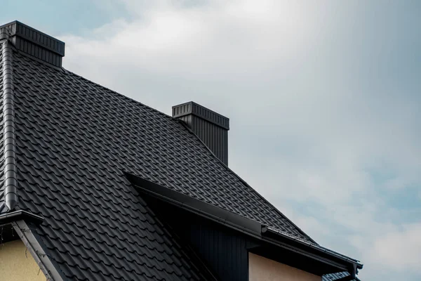 Techo de baldosas de metal negro. Chapas de metal de techo. Tipos modernos de materiales para techos. Techo de la casa, teja de metal contra el cielo azul. Edificio . —  Fotos de Stock