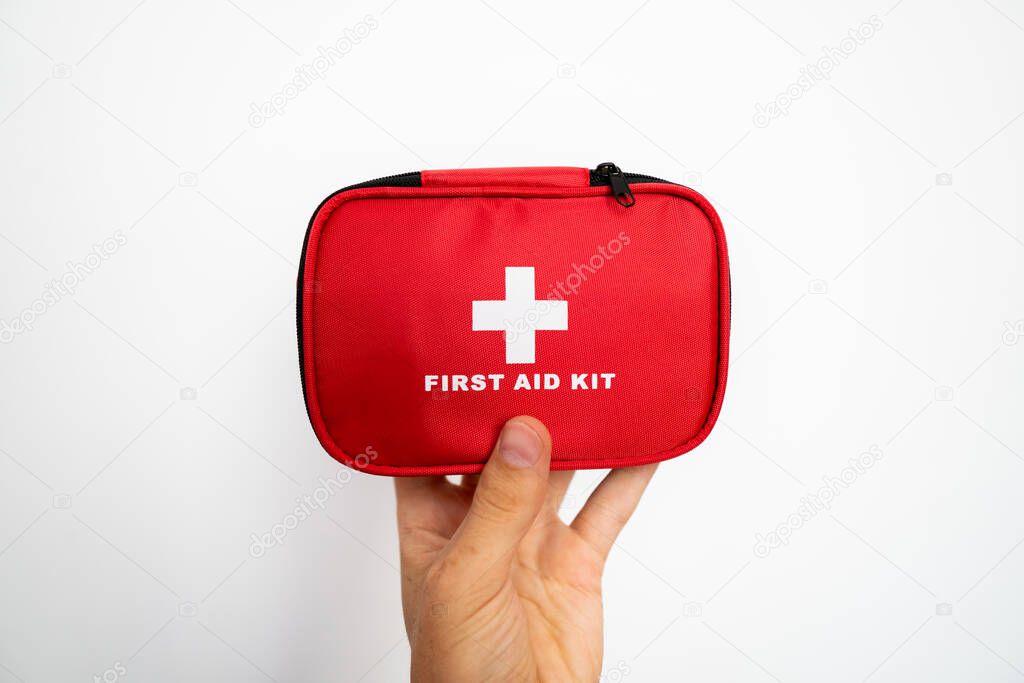 Mans hand holding a red first-aid kit with a white wall on background.