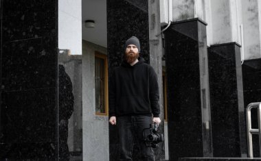 Siyah kapüşonlu sakallı profesyonel kameraman elinde 3 eksenli titreşim dengeleyicisi var. Film yapımcısı profesyonel bir sinema kamerasıyla harika bir video çekiyor. Görüntü Yönetmeni.
