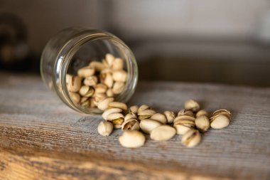 Fıstıklar bir kavanozun içindeki beyaz şarap masasına saçılmış. Pistachio sağlıklı bir vejetaryen protein yiyeceğidir. Köhne odunlarda fıstıklar.