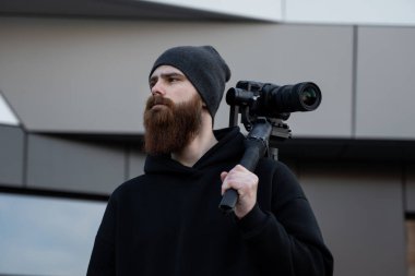 Siyah kapüşonlu sakallı profesyonel kameraman elinde 3 eksenli titreşim dengeleyicisi var. Film yapımcısı profesyonel bir sinema kamerasıyla harika bir video çekiyor. Görüntü Yönetmeni.