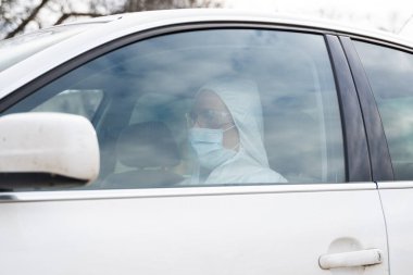 Koruyucu giysili, tıbbi maskeli ve plastik eldivenli bir adam bakteri ve virüsten korunmayı planlıyor. Karantina sırasında koruyucu maske, dünya salgını, covid 19, koronavirüs, enfeksiyon.